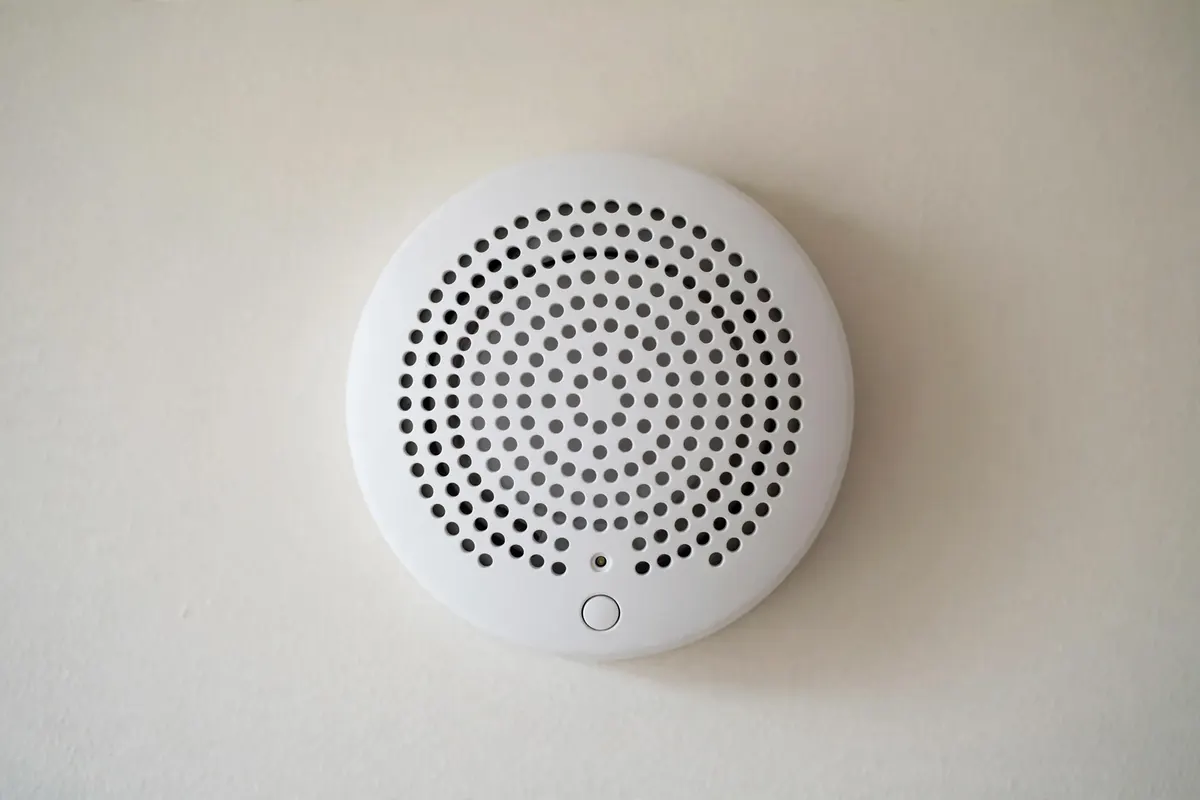 A close-up of a white carbon monoxide detector on a plain hallway wall